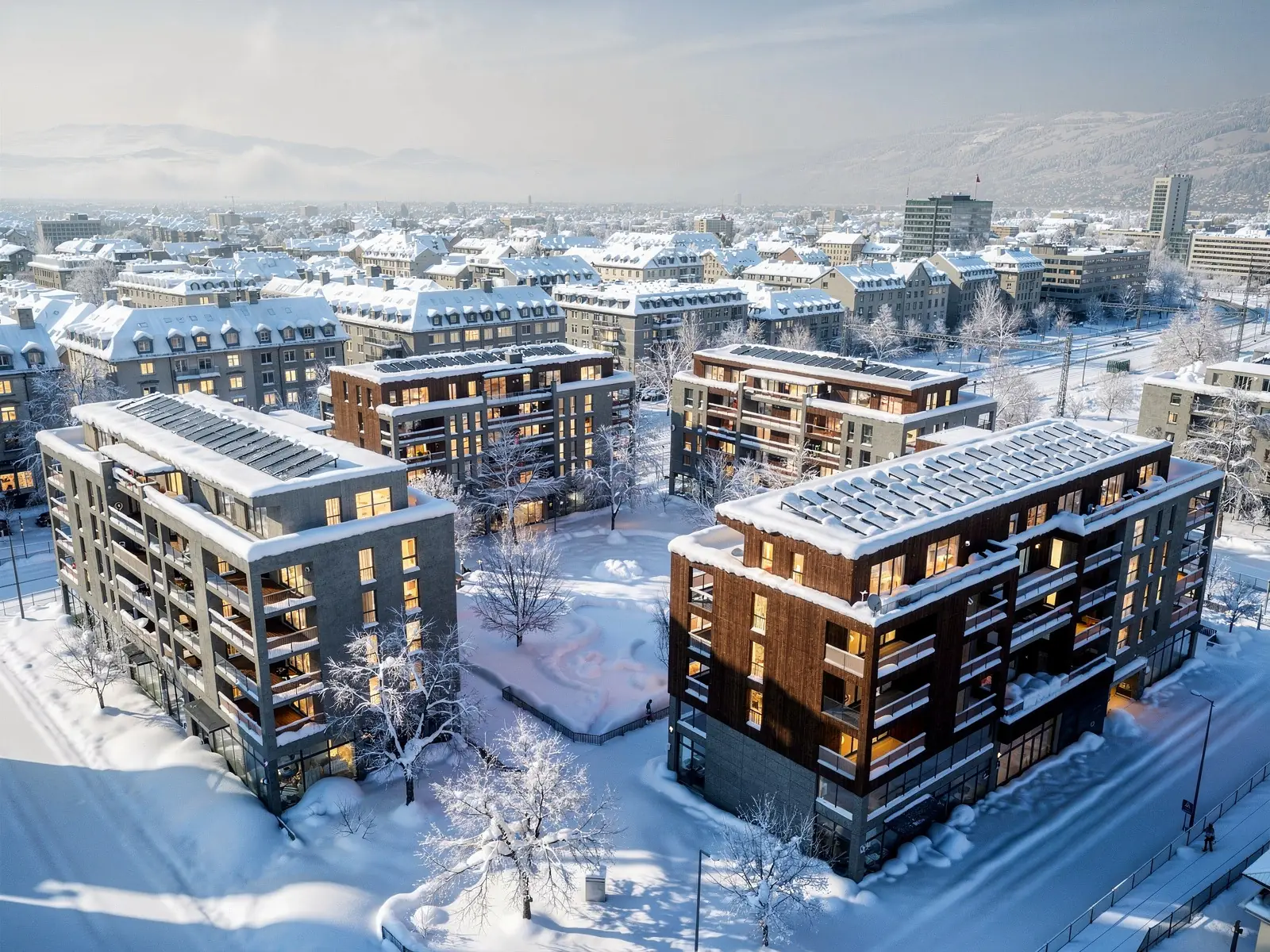 Luftaufnahme eines Schweizer Areals mit sechs Wohn- und Geschäftsgebäuden um einen begrünten Innenhof, Photovoltaik auf allen Dächern, im Winter
