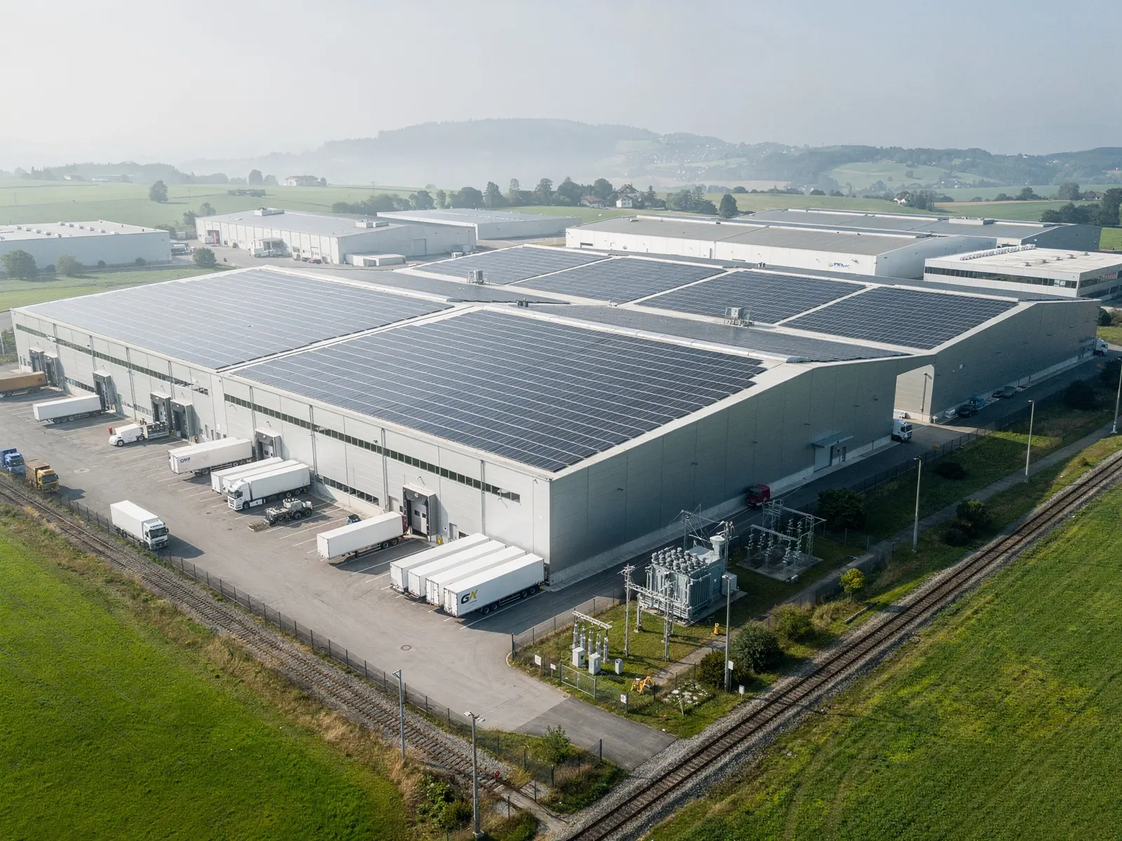 Luftaufnahme eines Schweizer Industrieareals mit grossflächiger Photovoltaik auf den Hallendächern und einem Unterwerk am Rand des Geländes
